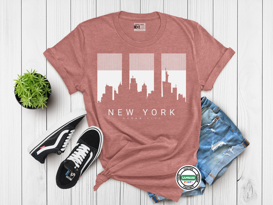 Pink t-shirt with New York cityscape design, paired with black sneakers and denim shorts on a wooden surface.