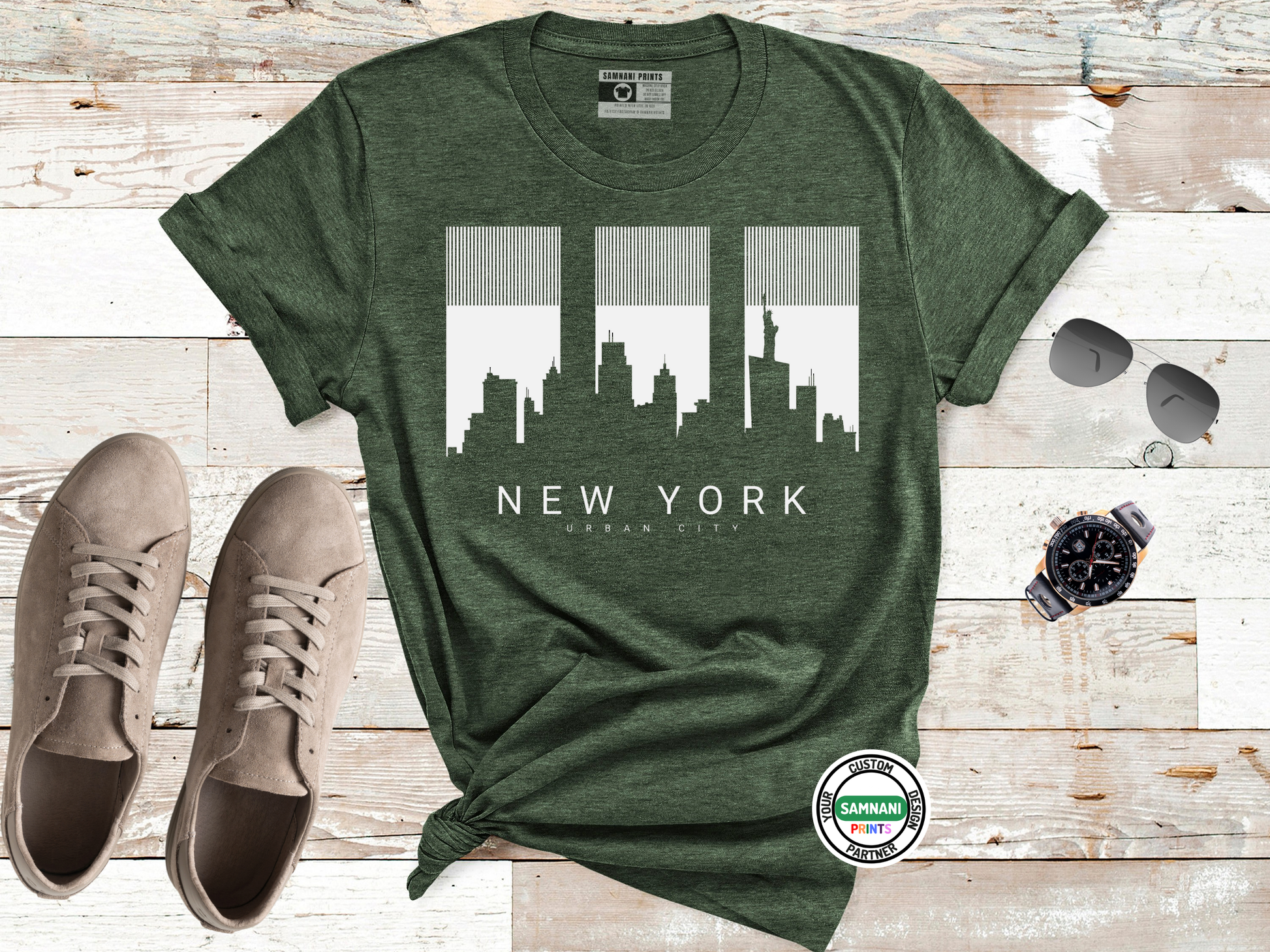 Green t-shirt with New York city skyline design on a wooden surface with shoes and a watch.