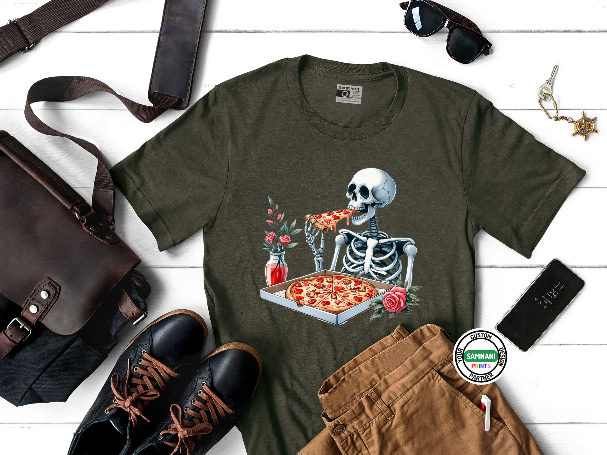 Black skeleton pizza shirt featuring a romantic undead dinner scene with heart-shaped pizza and roses, styled on white wooden background with leather accessories and sunglasses, great alt fashion.