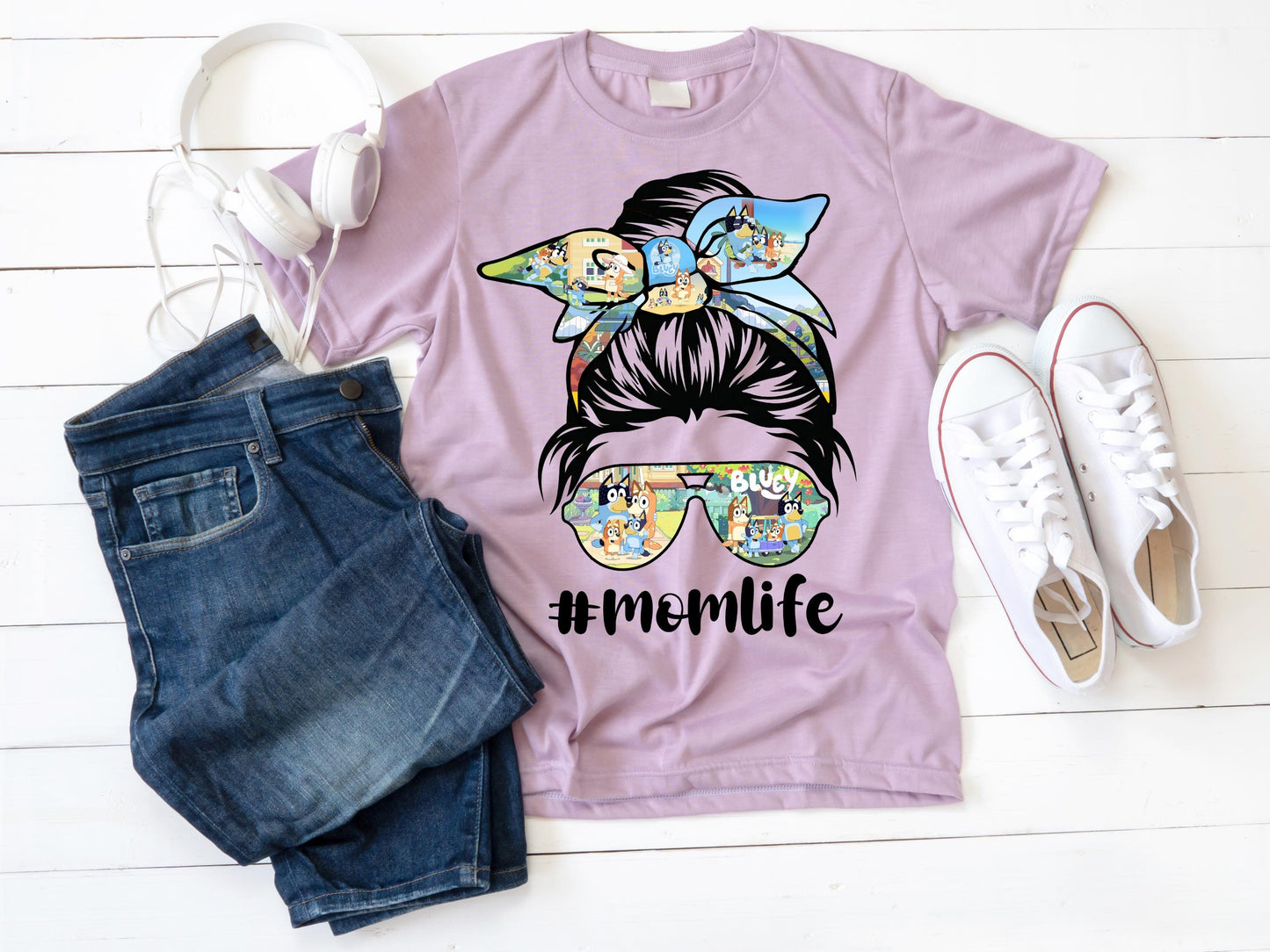 A flat lay t shirt a trendy light purple color "Mom Life" t-shirt featuring a messy bun with a Bluey-themed bow and sunglasses, along with the hashtag #MomLife in black text. The stylish and fun design makes it a perfect casual outfit for moms who love cartoons and playful fashion. The woman is accessorized with bracelets and a necklace, adding to the trendy aesthetic.