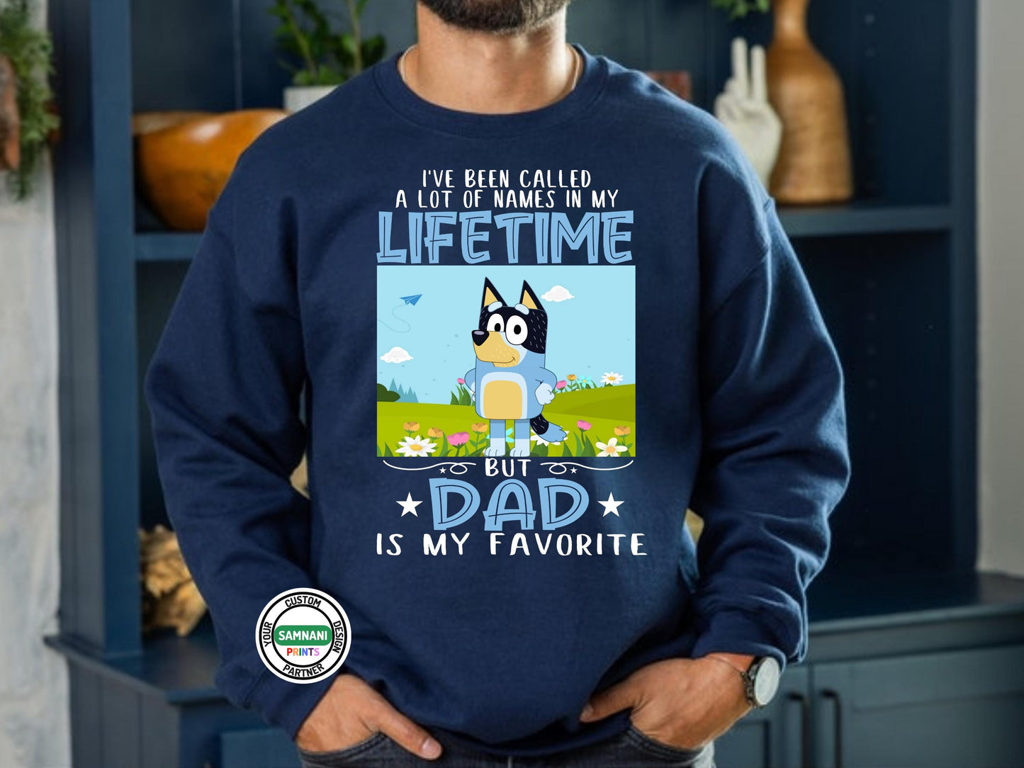 A man wearing a navy blue sweatshirt with a cartoon dad character in a field of flowers and text that reads “I’ve Been Called a Lot of Names in My Lifetime, But Dad Is My Favorite.”Father’s Day Gift from Kids – Bluey Cartoon Tee for Dad – Dad Is My Favorite Shirt. Father's Day gift, gift for dad, gift for paw paw, gift for father. Bluey Bandit T-shirt and sweatshirt.